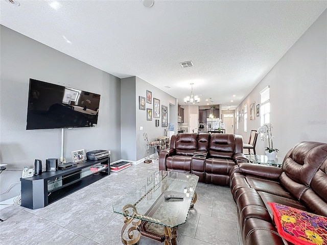 living area featuring visible vents, a notable chandelier, a textured ceiling, and baseboards