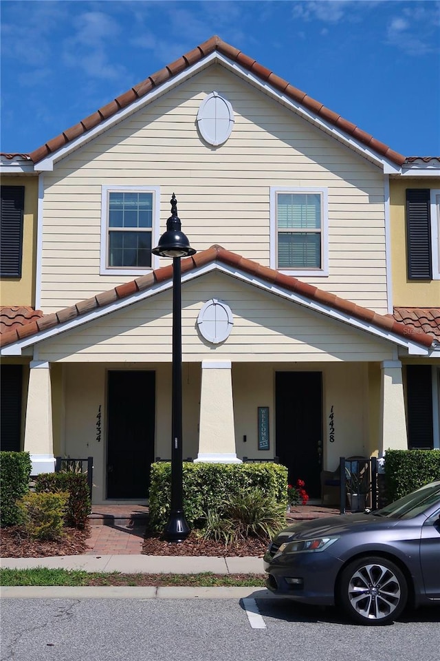 view of property with stucco siding, a porch, and a tiled roof