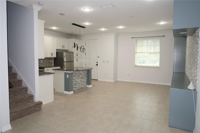 kitchen featuring dark stone countertops, a kitchen island, freestanding refrigerator, and ornamental molding