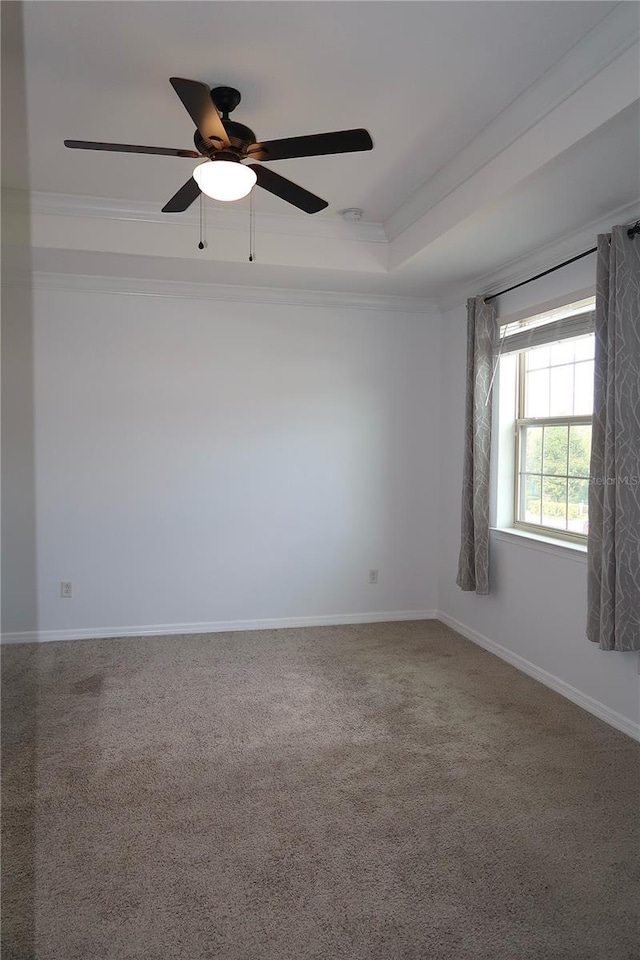 carpeted empty room featuring ceiling fan, a tray ceiling, baseboards, and ornamental molding