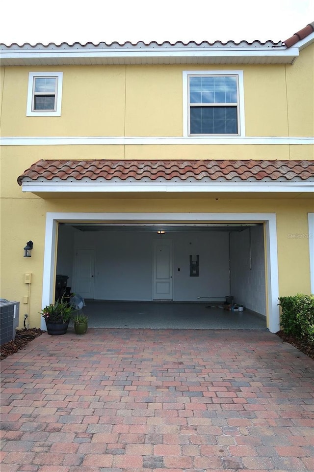 garage with electric panel, decorative driveway, and cooling unit