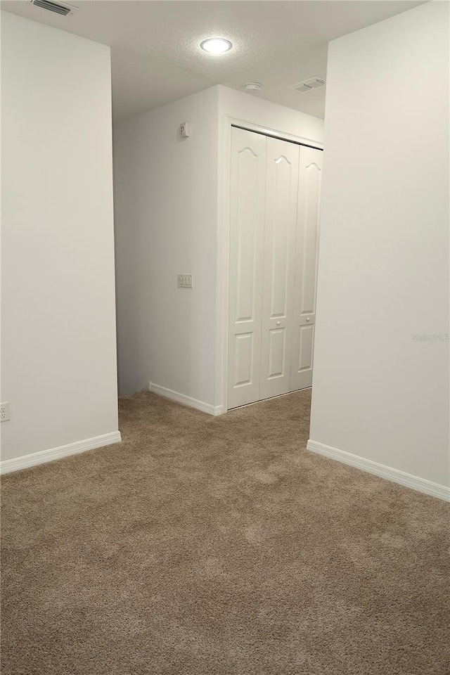 carpeted spare room featuring visible vents, a textured ceiling, and baseboards