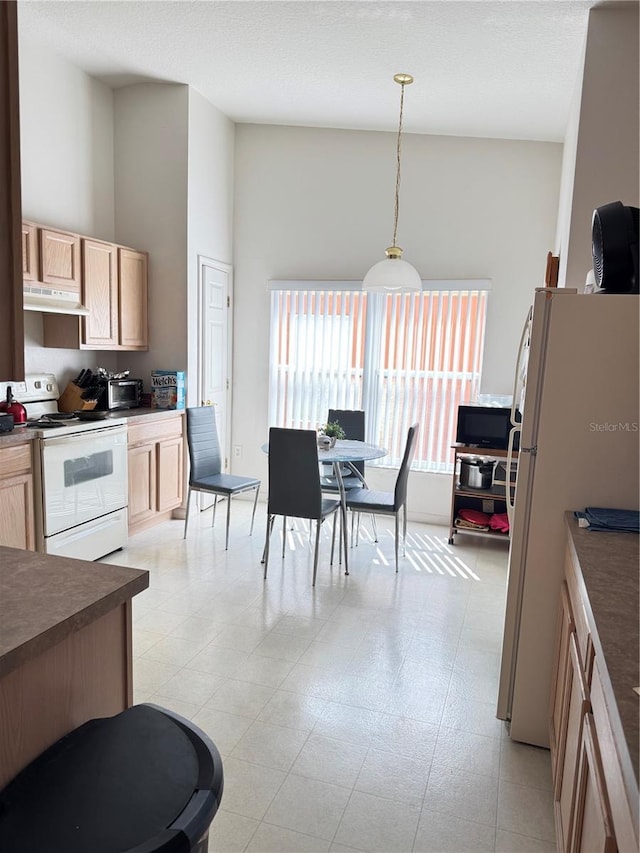 kitchen with dark countertops, a high ceiling, light brown cabinets, white appliances, and under cabinet range hood