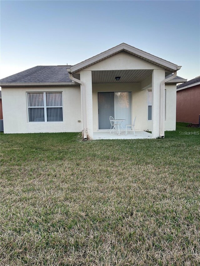 back of property featuring roof with shingles, a patio area, a lawn, and stucco siding