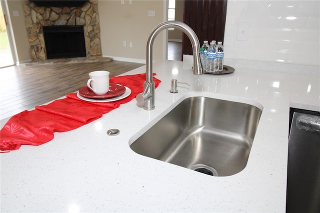 interior details with dishwashing machine, a stone fireplace, wood finished floors, a sink, and light countertops