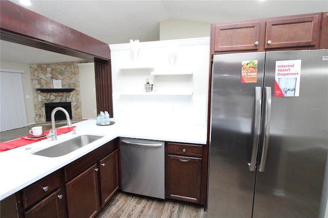 kitchen with stainless steel appliances, light countertops, a sink, and a stone fireplace