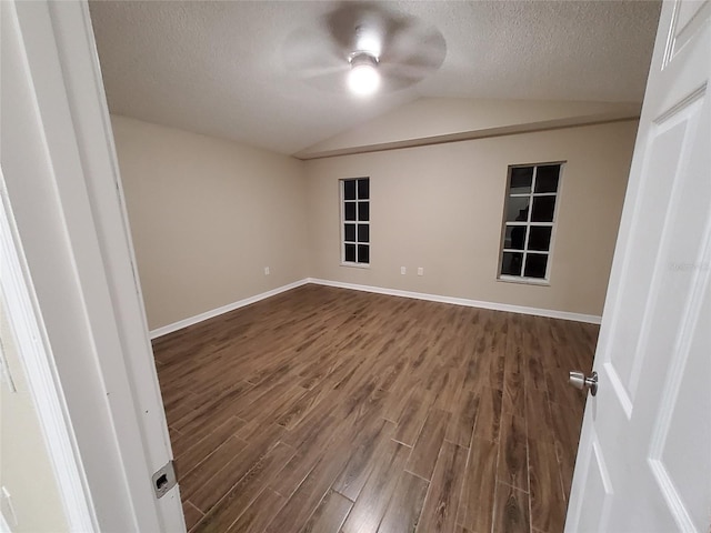 empty room featuring baseboards, a ceiling fan, dark wood-style floors, vaulted ceiling, and a textured ceiling