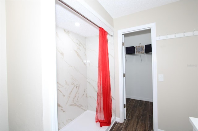 full bath featuring baseboards, a textured ceiling, a marble finish shower, and wood finished floors