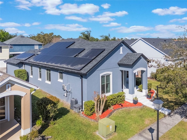 view of front facade featuring a front yard, roof with shingles, roof mounted solar panels, and stucco siding