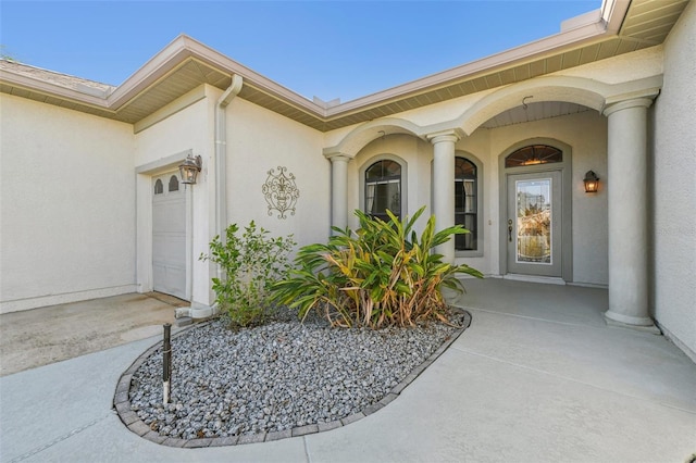 entrance to property featuring a garage, concrete driveway, and stucco siding