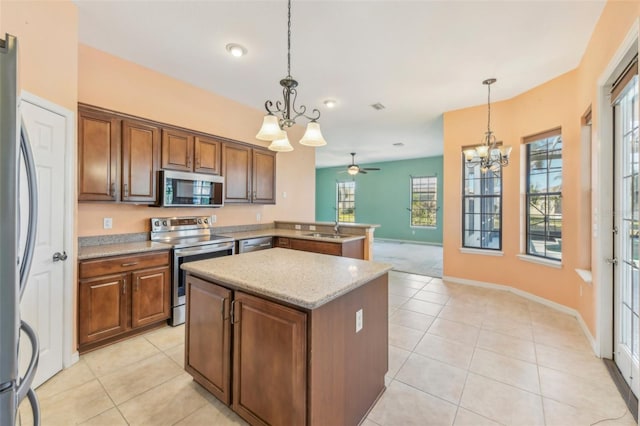 kitchen with light stone counters, a center island, hanging light fixtures, stainless steel appliances, and a sink