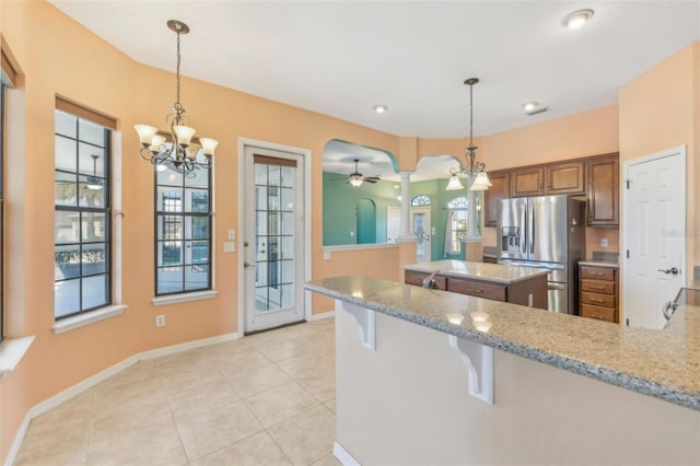 kitchen featuring light stone counters, arched walkways, stainless steel refrigerator with ice dispenser, a peninsula, and a kitchen breakfast bar