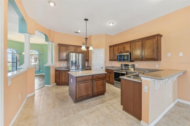 kitchen featuring a breakfast bar area, a peninsula, appliances with stainless steel finishes, decorative light fixtures, and ornate columns