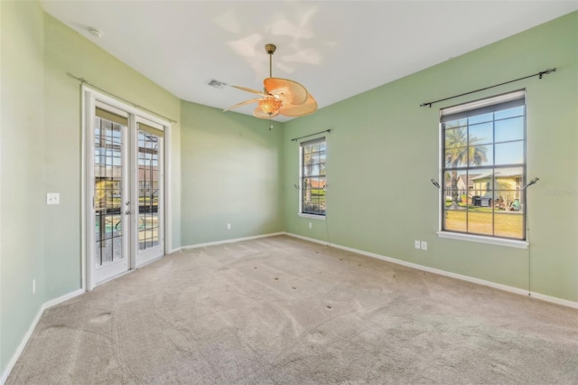 unfurnished room featuring french doors, light colored carpet, visible vents, a ceiling fan, and baseboards