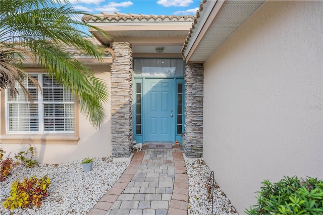 doorway to property with stone siding, a tile roof, and stucco siding