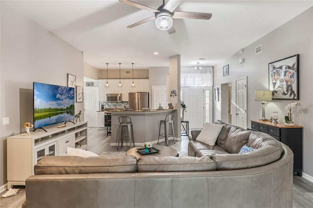 living room with light wood-style floors, visible vents, baseboards, and a ceiling fan