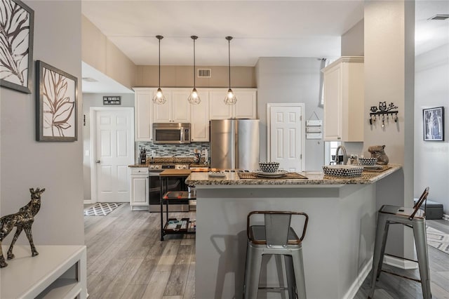 kitchen with visible vents, appliances with stainless steel finishes, light wood-type flooring, tasteful backsplash, and dark stone countertops