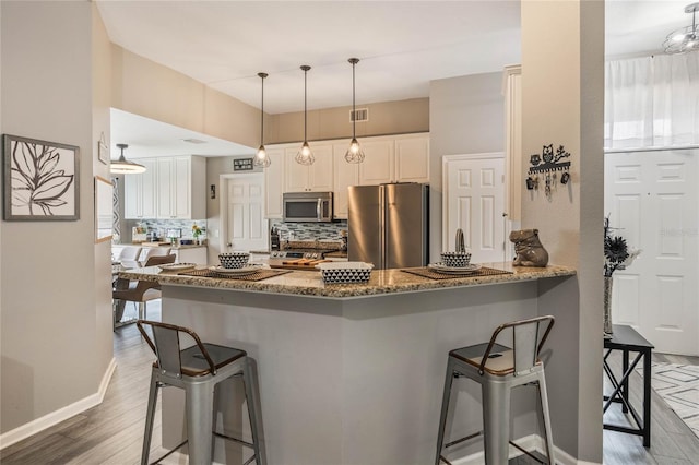 kitchen with stainless steel appliances, stone counters, light wood-style flooring, and a kitchen breakfast bar