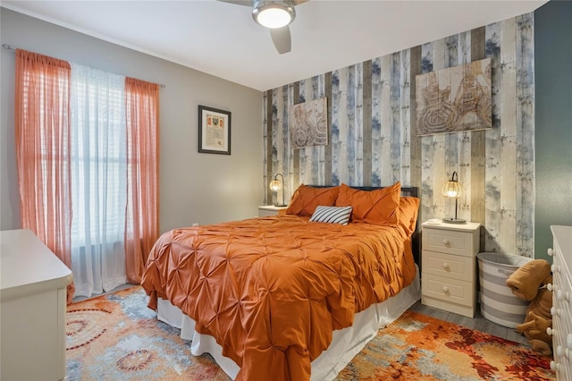 bedroom with ceiling fan, an accent wall, wood finished floors, and wallpapered walls