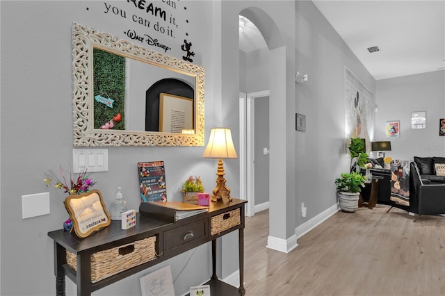 corridor featuring arched walkways, visible vents, light wood-style flooring, and baseboards