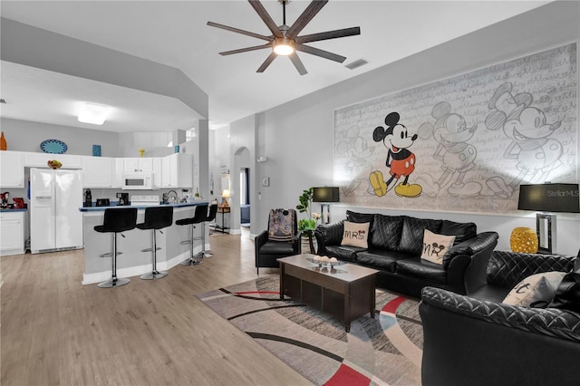 living area featuring arched walkways, a ceiling fan, visible vents, vaulted ceiling, and light wood-style floors