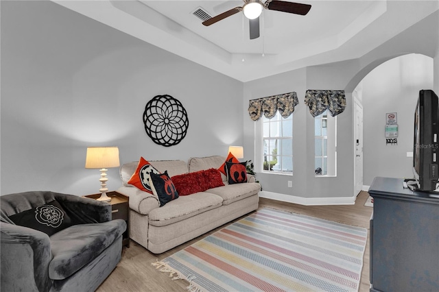 living area featuring arched walkways, wood finished floors, visible vents, baseboards, and a tray ceiling