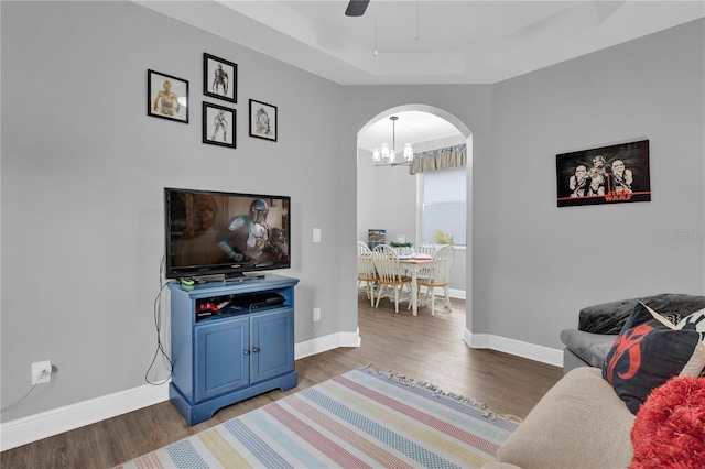 living area with arched walkways, dark wood-style flooring, ceiling fan with notable chandelier, and baseboards