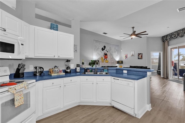 kitchen featuring a peninsula, white appliances, a sink, white cabinets, and dark countertops