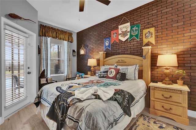 bedroom with light wood-type flooring, access to exterior, brick wall, and ceiling fan