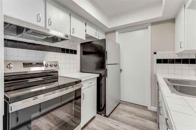 kitchen featuring light wood finished floors, electric range, tile countertops, freestanding refrigerator, and under cabinet range hood