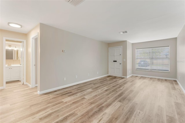 spare room featuring light wood finished floors, visible vents, and baseboards