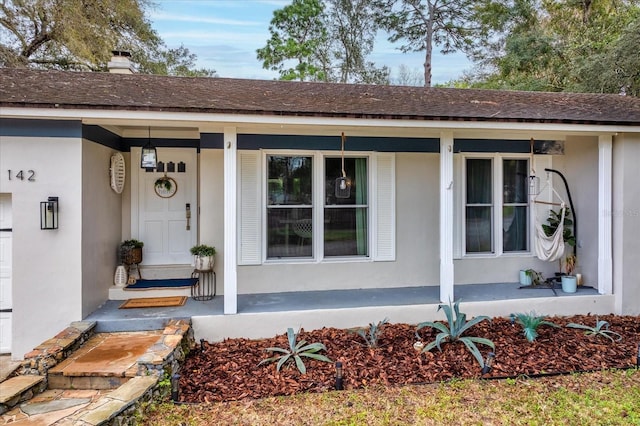 entrance to property with a porch, a chimney, and stucco siding