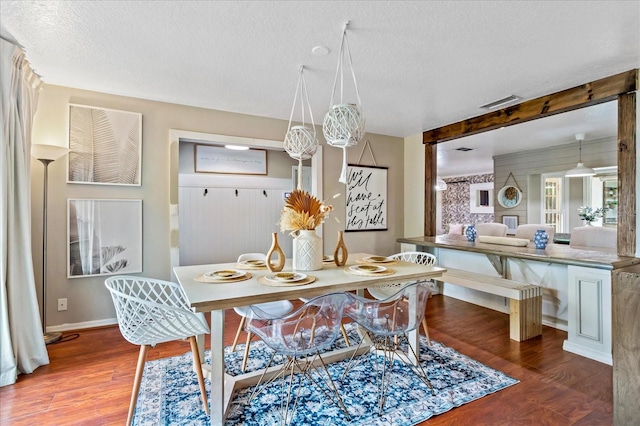 dining room featuring a textured ceiling, visible vents, wood finished floors, and beamed ceiling