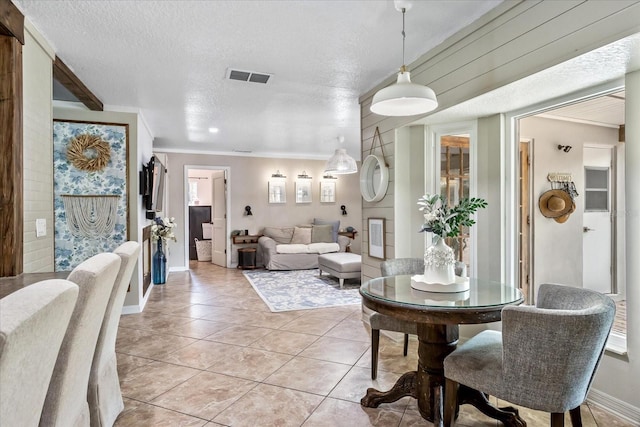 dining area with a textured ceiling, light tile patterned floors, visible vents, baseboards, and crown molding