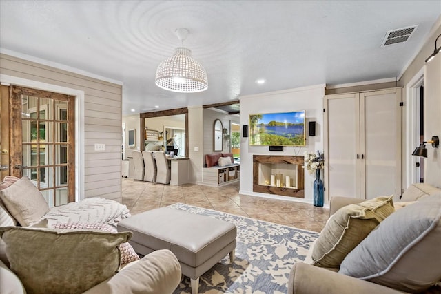 living room featuring a warm lit fireplace, light tile patterned flooring, recessed lighting, wooden walls, and visible vents