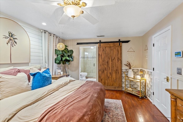 bedroom with a barn door, visible vents, hardwood / wood-style flooring, ensuite bathroom, and a textured ceiling