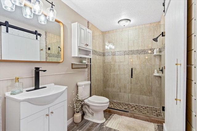 full bath featuring a textured ceiling, toilet, wood finished floors, vanity, and a shower stall