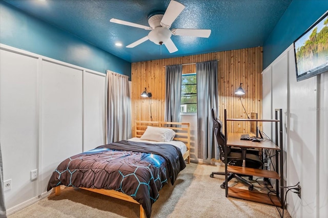 carpeted bedroom with wood walls, ceiling fan, and a textured ceiling