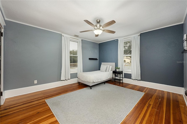 bedroom with a ceiling fan, visible vents, baseboards, ornamental molding, and dark wood finished floors