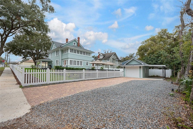 view of front facade featuring a fenced front yard, a chimney, a garage, a carport, and driveway