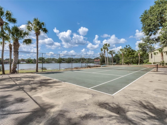 view of tennis court with a water view and fence