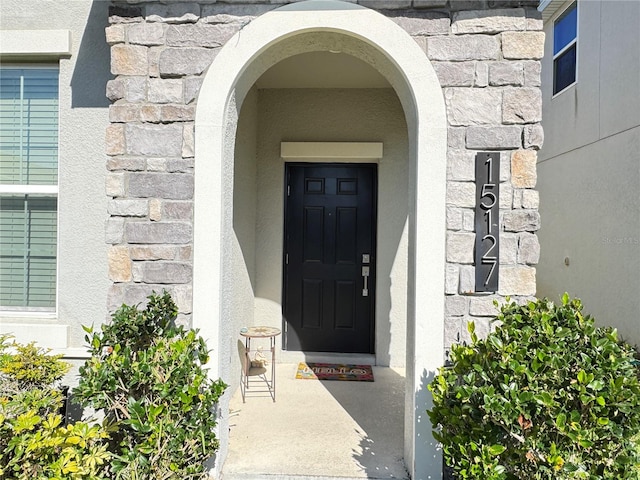 view of exterior entry featuring stone siding and stucco siding