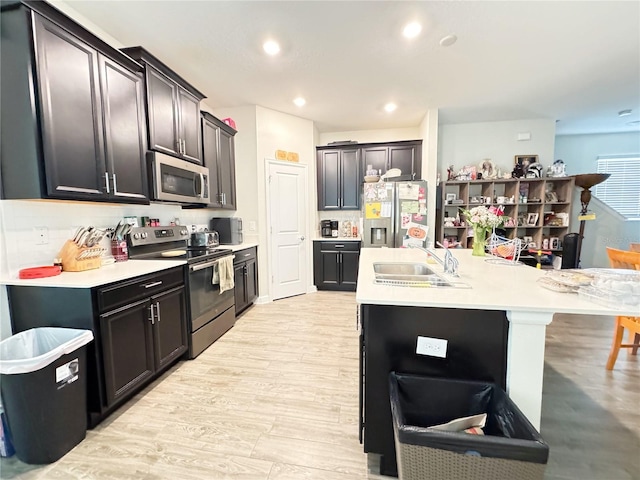 kitchen featuring a breakfast bar area, stainless steel appliances, a sink, light countertops, and an island with sink