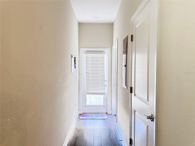 hall featuring a textured wall, baseboards, and wood finished floors