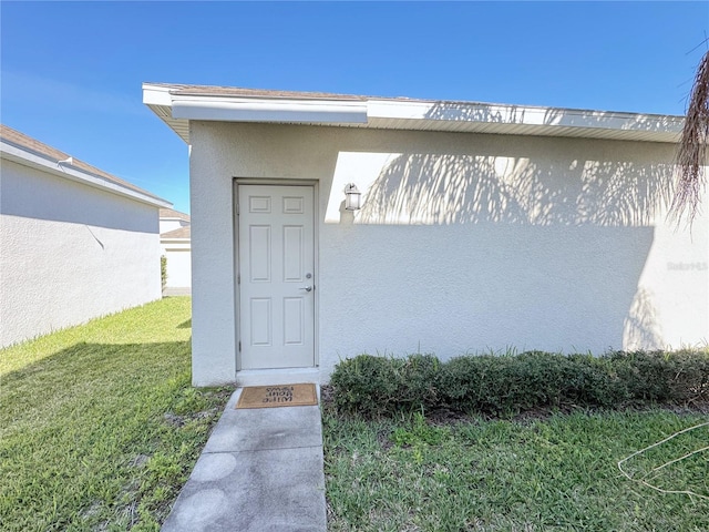 doorway to property with a lawn and stucco siding