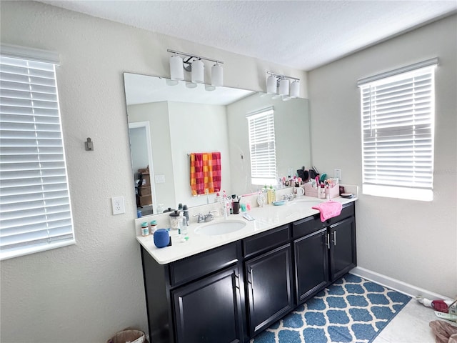 full bath with baseboards, double vanity, a sink, and a healthy amount of sunlight