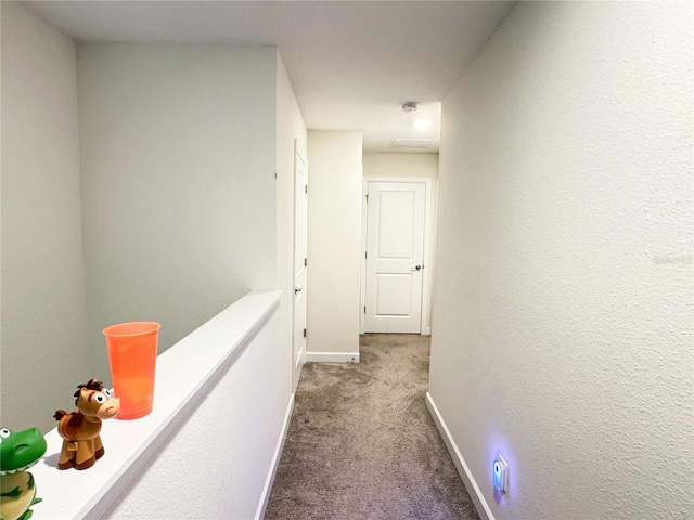 corridor featuring light carpet, a textured wall, and baseboards