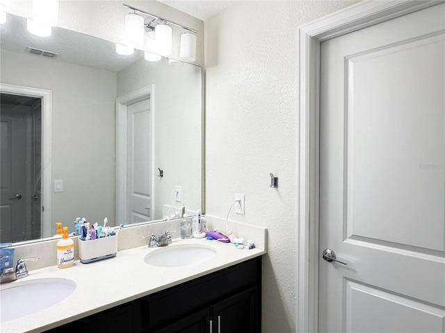 bathroom featuring double vanity, visible vents, a sink, and a textured wall