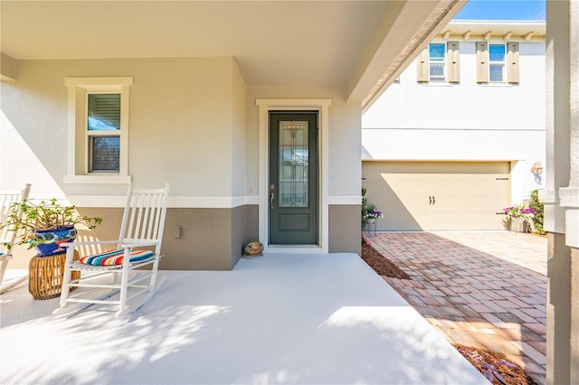 view of exterior entry with a garage, decorative driveway, and stucco siding