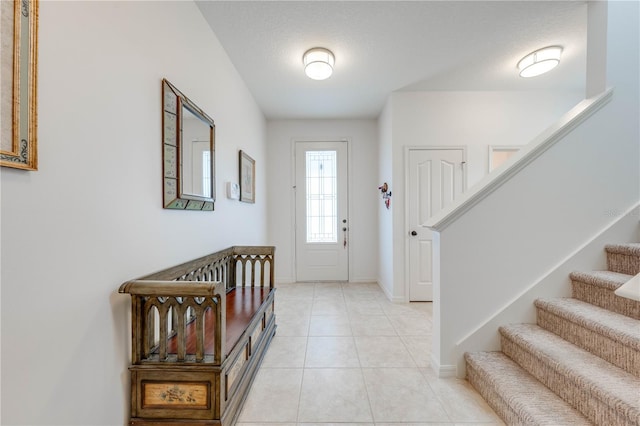 entrance foyer featuring stairs, light tile patterned floors, a textured ceiling, and baseboards